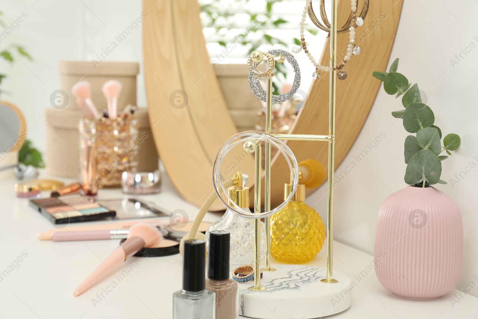 Photo of Makeup room. Mirror, jewelry and different cosmetic products on white dressing table indoors, closeup