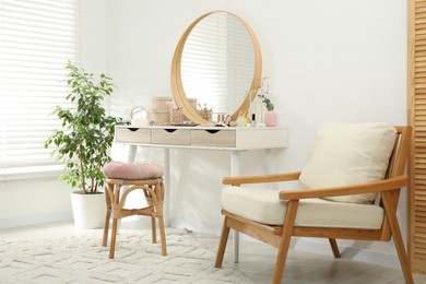 Photo of Makeup room. Dressing table with mirror, different beauty products, stool, armchair and houseplant indoors