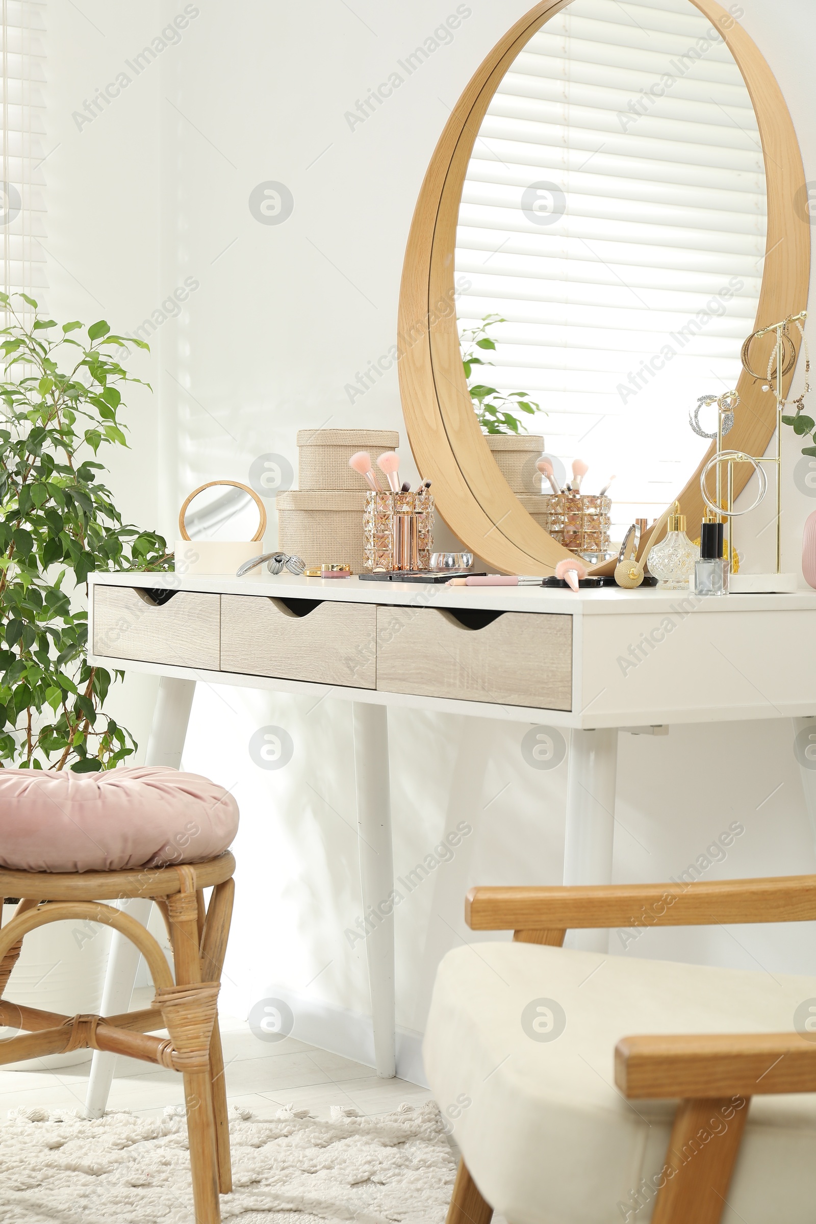 Photo of Makeup room. Dressing table with mirror, different beauty products, stool, armchair and houseplant indoors