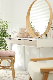 Photo of Makeup room. Dressing table with mirror, different beauty products, stool, armchair and houseplant indoors