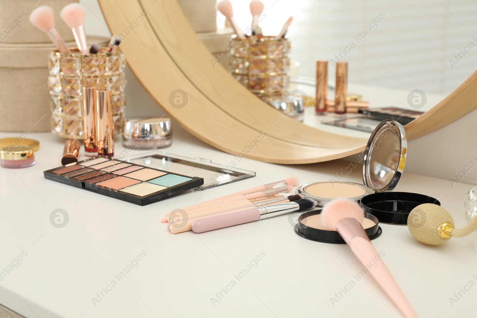 Photo of Makeup room. Mirror and different cosmetic products on white dressing table indoors, closeup