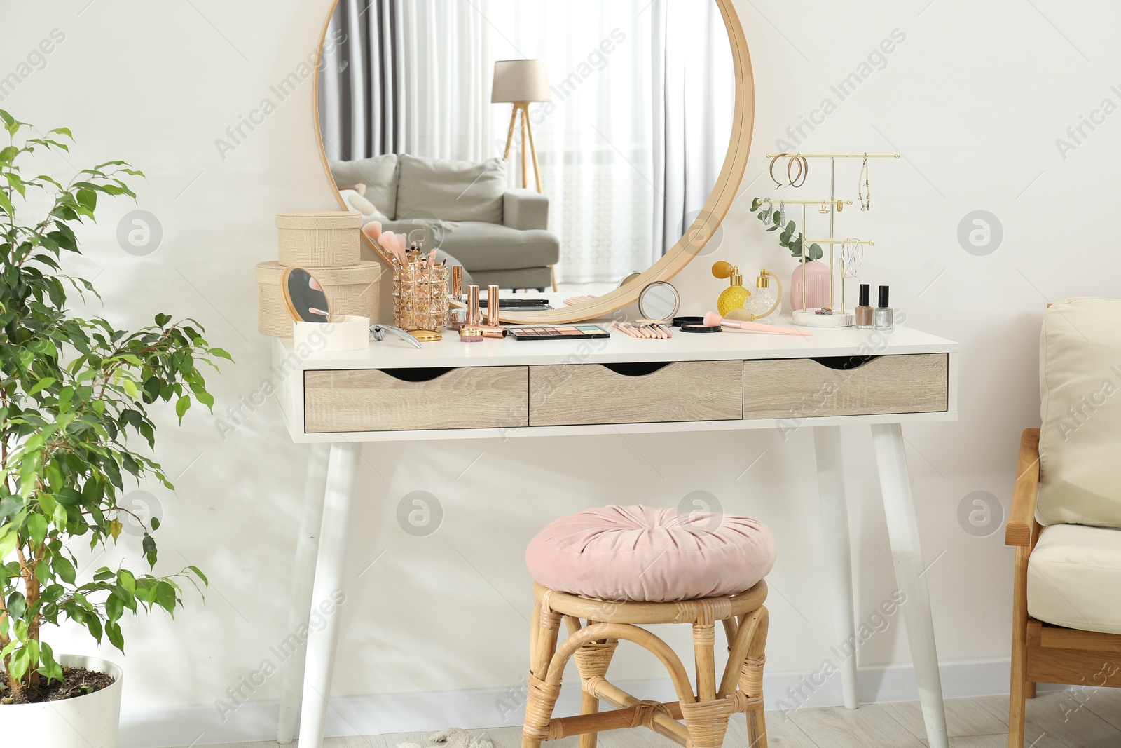 Photo of Makeup room. Dressing table with mirror, different beauty products, stool, armchair and houseplant