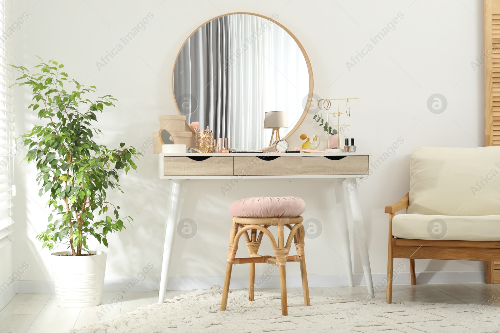 Photo of Makeup room. Dressing table with mirror, different beauty products, stool, armchair and houseplant