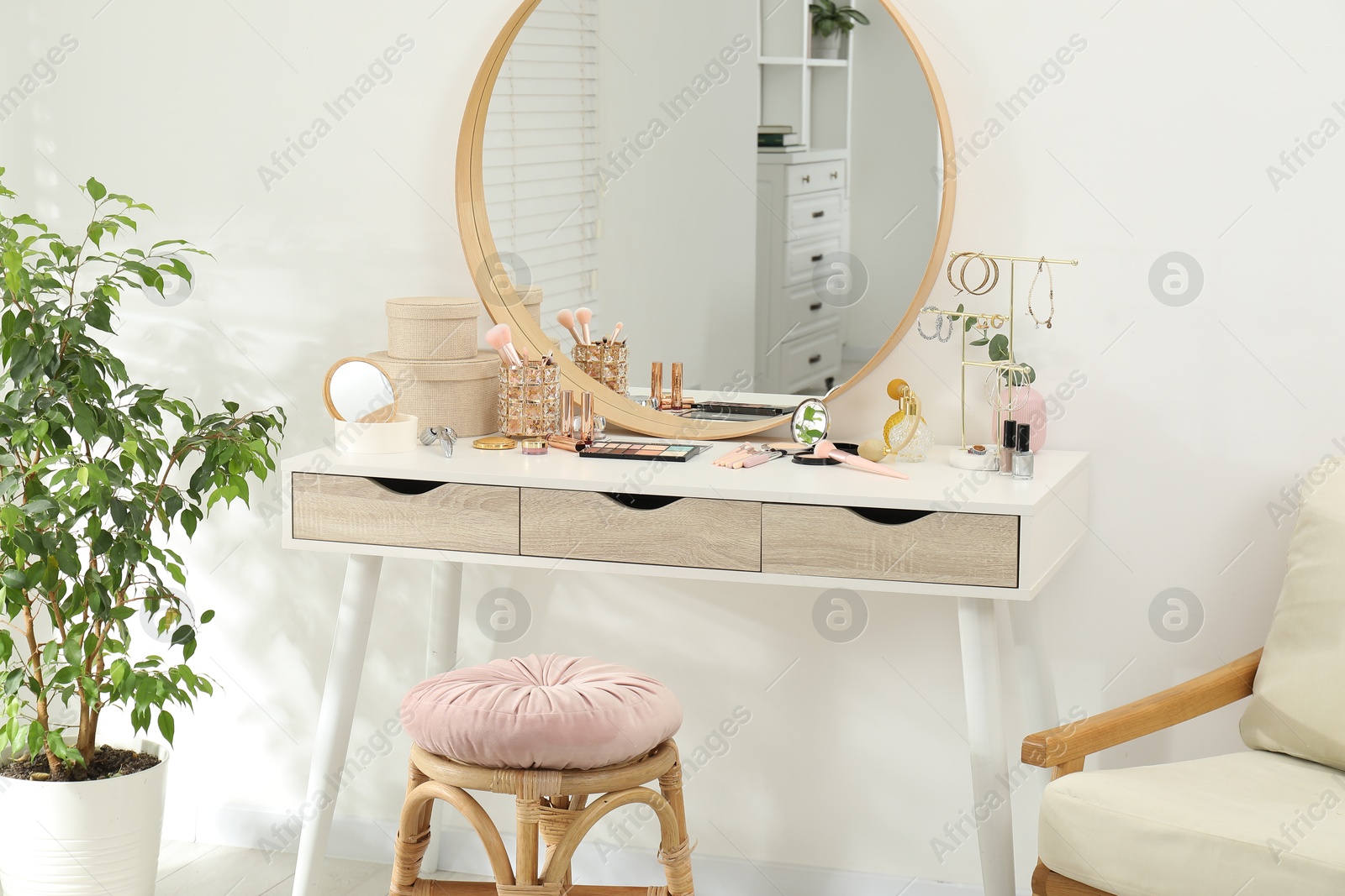 Photo of Makeup room. Dressing table with mirror, different beauty products, stool, armchair and houseplant