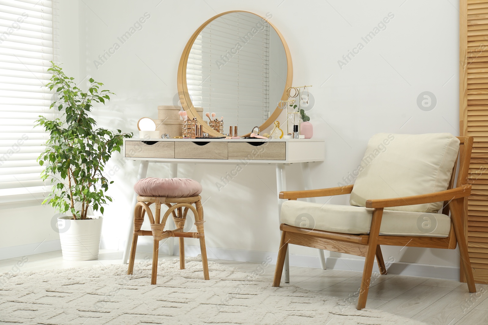 Photo of Makeup room. Dressing table with mirror, different beauty products, stool, armchair and houseplant