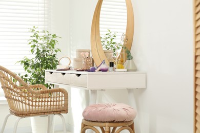 Photo of Makeup room. Dressing table with mirror, different beauty products, jewelry, chair and houseplant indoors