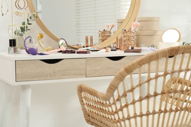 Photo of Makeup room. Dressing table with mirror, different beauty products, jewelry and chair indoors