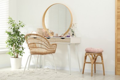 Photo of Makeup room. Dressing table with mirror, different beauty products, jewelry, chair and houseplant indoors