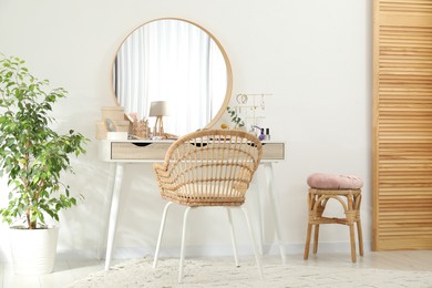 Photo of Makeup room. Dressing table with mirror, different beauty products, jewelry, chair and houseplant indoors