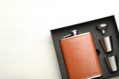 Photo of Hip flask, cups and funnel in package on light wooden table, top view. Space for text