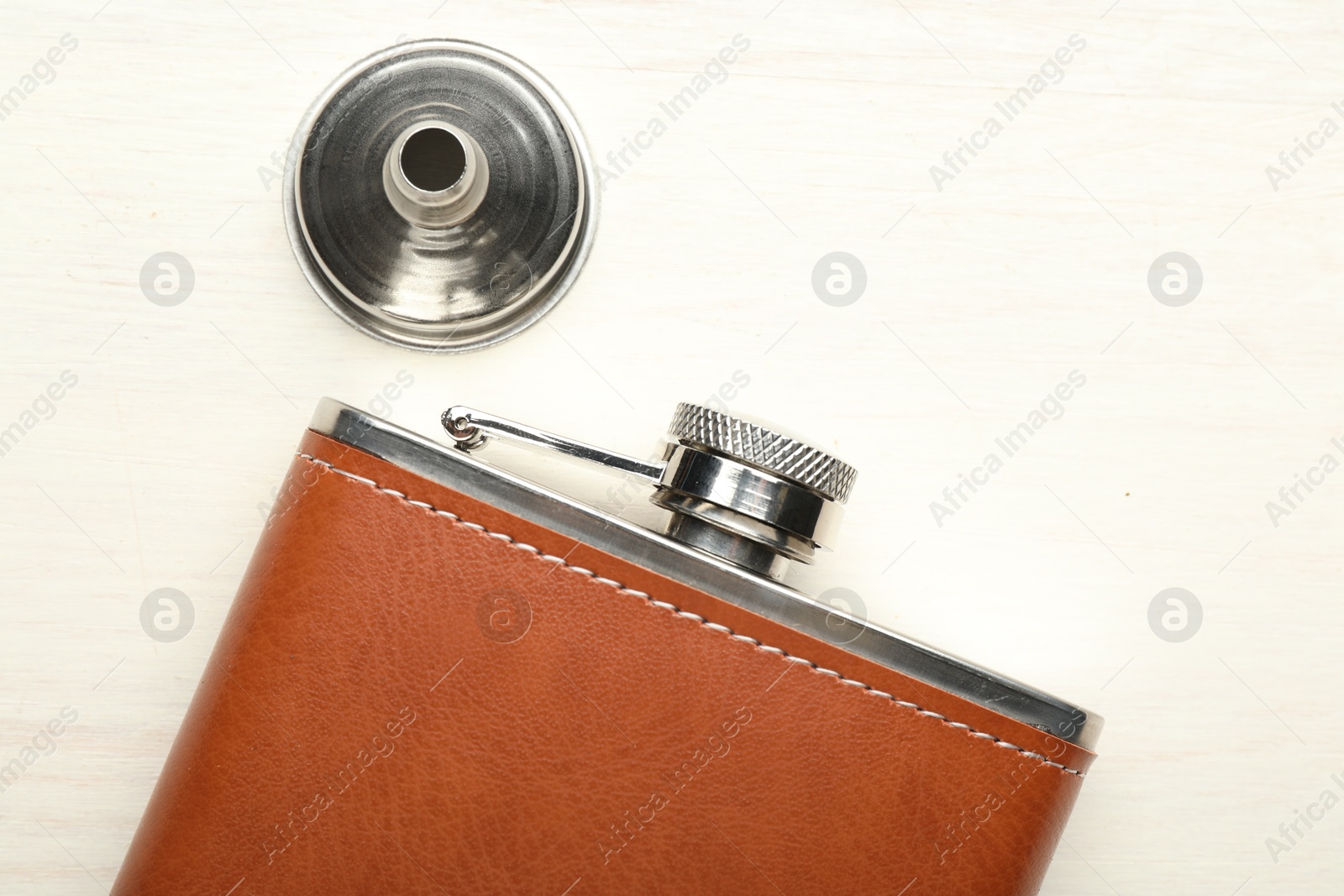 Photo of Hip flask and funnel on light wooden table, flat lay