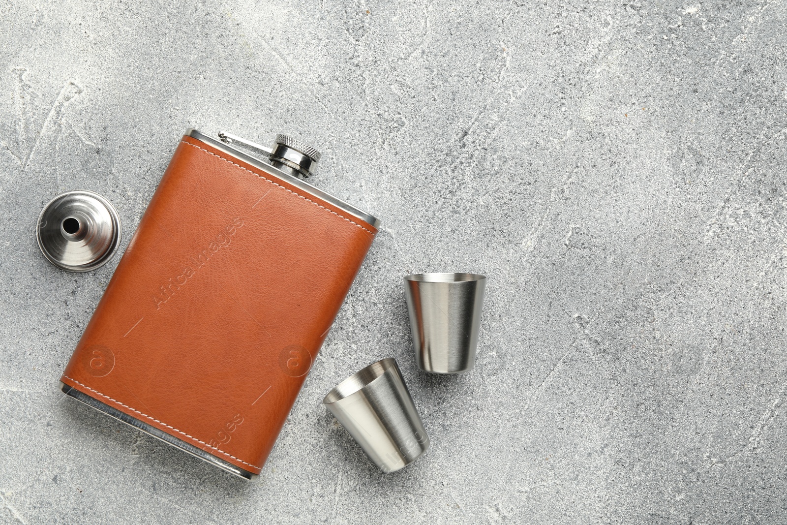 Photo of Hip flask, cups and funnel on grey textured table, flat lay. Space for text