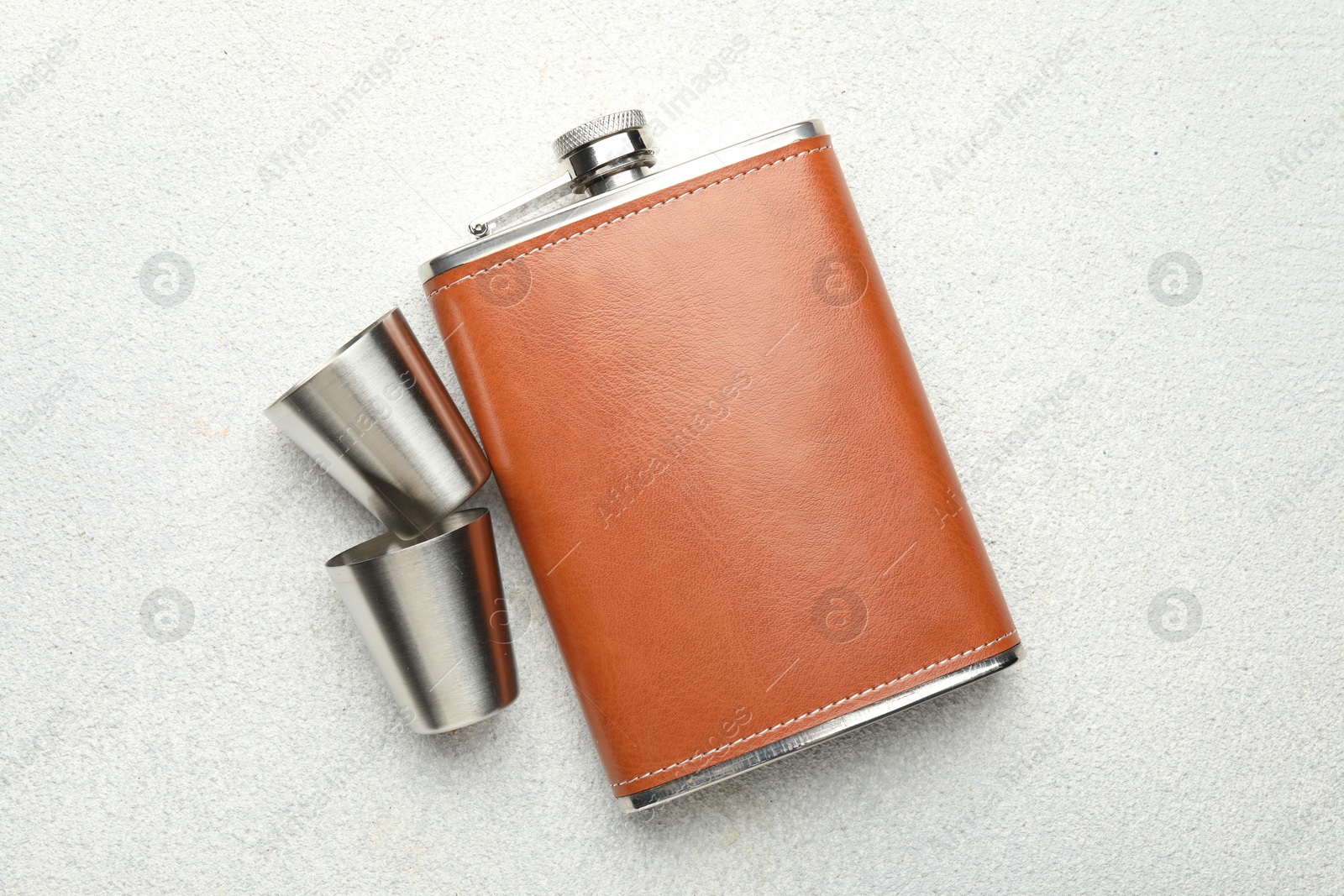 Photo of Hip flask and cups on light grey table, flat lay