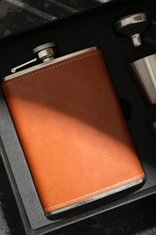 Photo of Hip flask, cup and funnel in package on dark table, top view