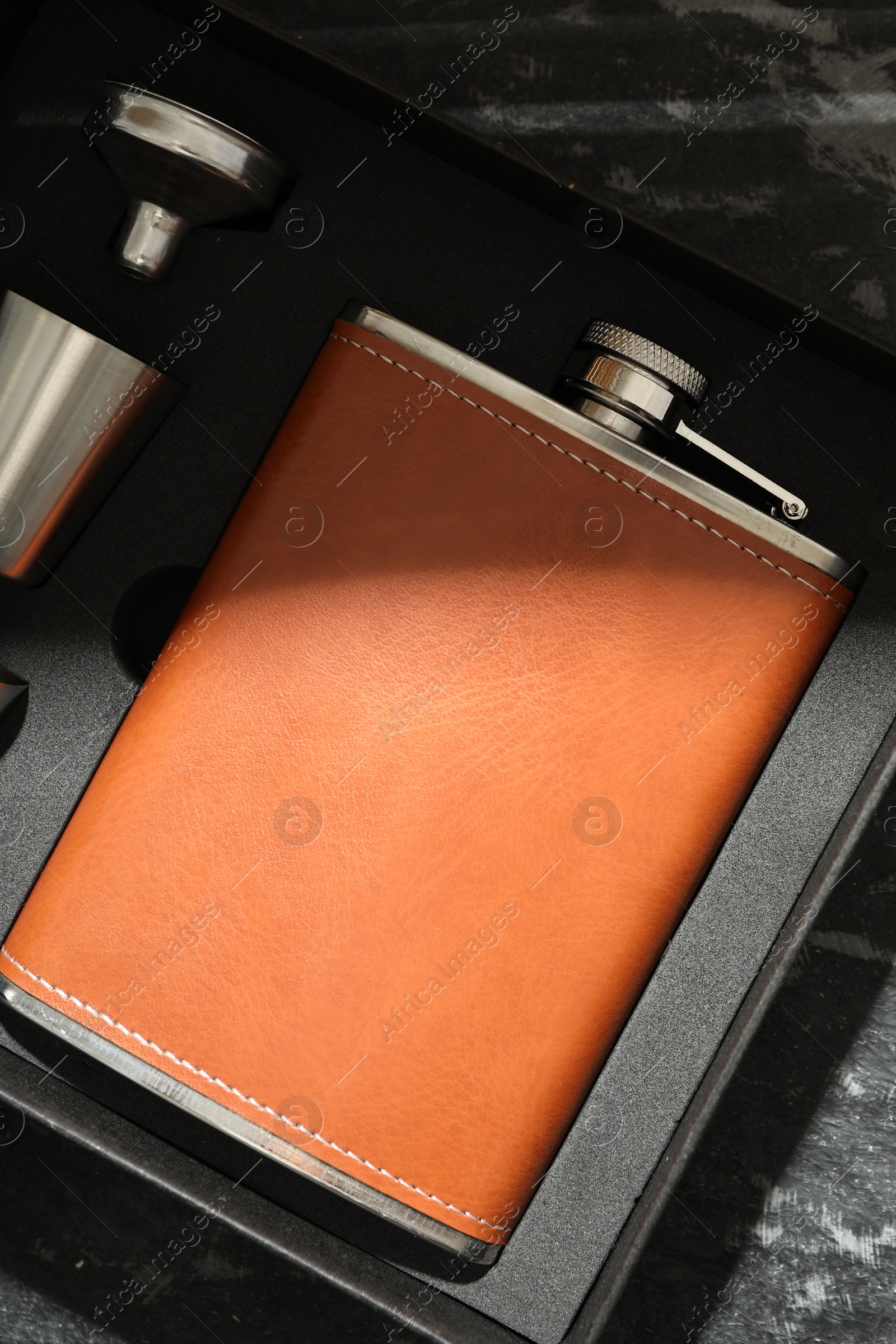 Photo of Hip flask, cup and funnel in package on dark table, top view