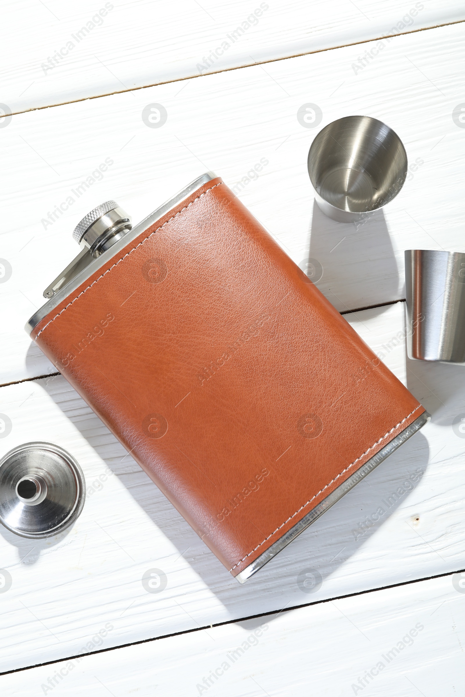 Photo of Hip flask, cups and funnel on white wooden table, flat lay