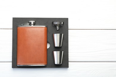 Photo of Hip flask, cups and funnel in package on white wooden table, top view. Space for text