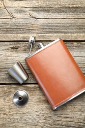 Photo of Hip flask, cup and funnel on wooden table, flat lay