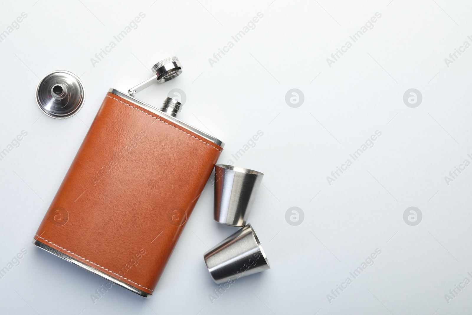 Photo of Hip flask, cups and funnel on white background, flat lay. Space for text