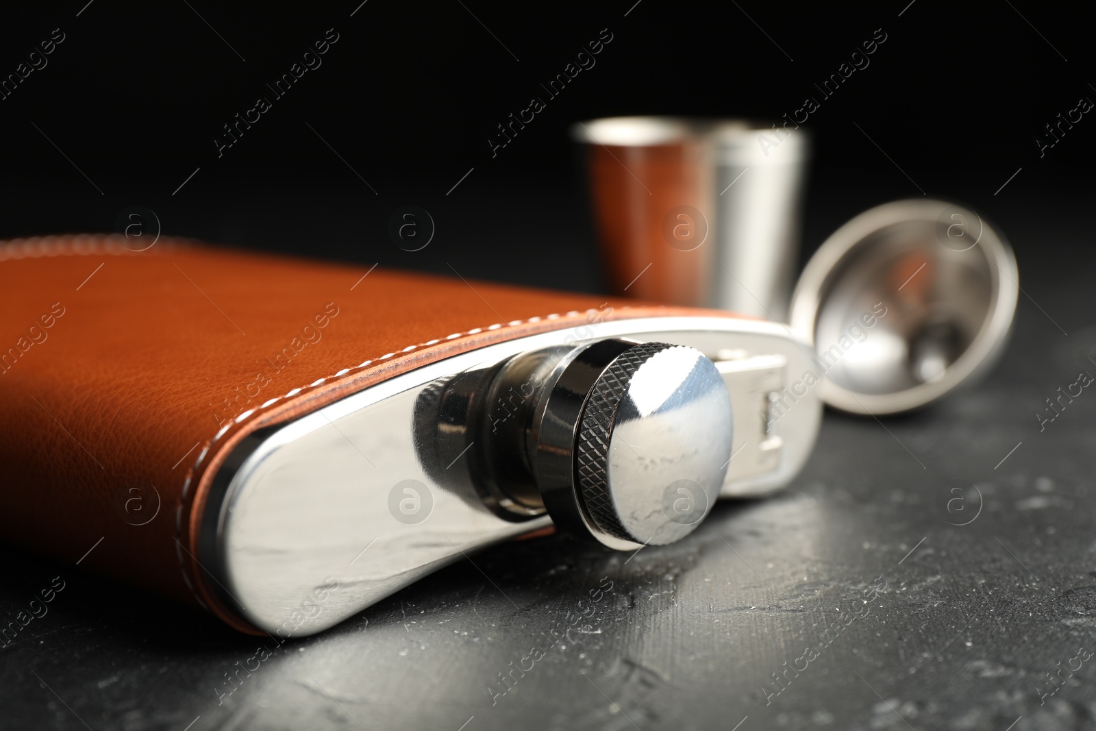 Photo of Hip flask, cup and funnel on black table, closeup