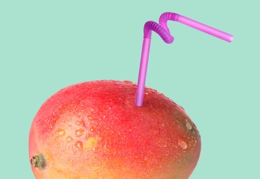 Image of Ripe mango with drinking straw on light turquoise background. Organic juice or freshly made smoothie concept