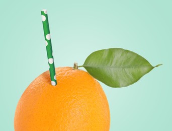 Image of Ripe orange with drinking straw on light turquoise background. Organic juice or freshly made smoothie concept