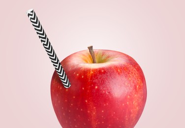 Image of Ripe red apple with drinking straw on pink grey background. Organic juice or freshly made smoothie concept