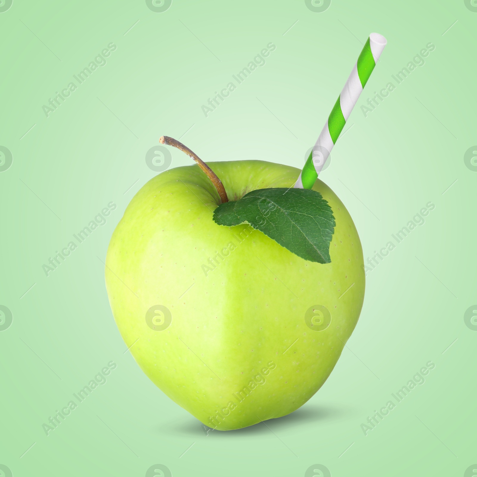 Image of Ripe apple with drinking straw on light green background. Organic juice or freshly made smoothie concept