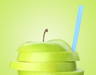 Image of Drinking straw in sliced apple on light green background. Organic juice or freshly made smoothie concept