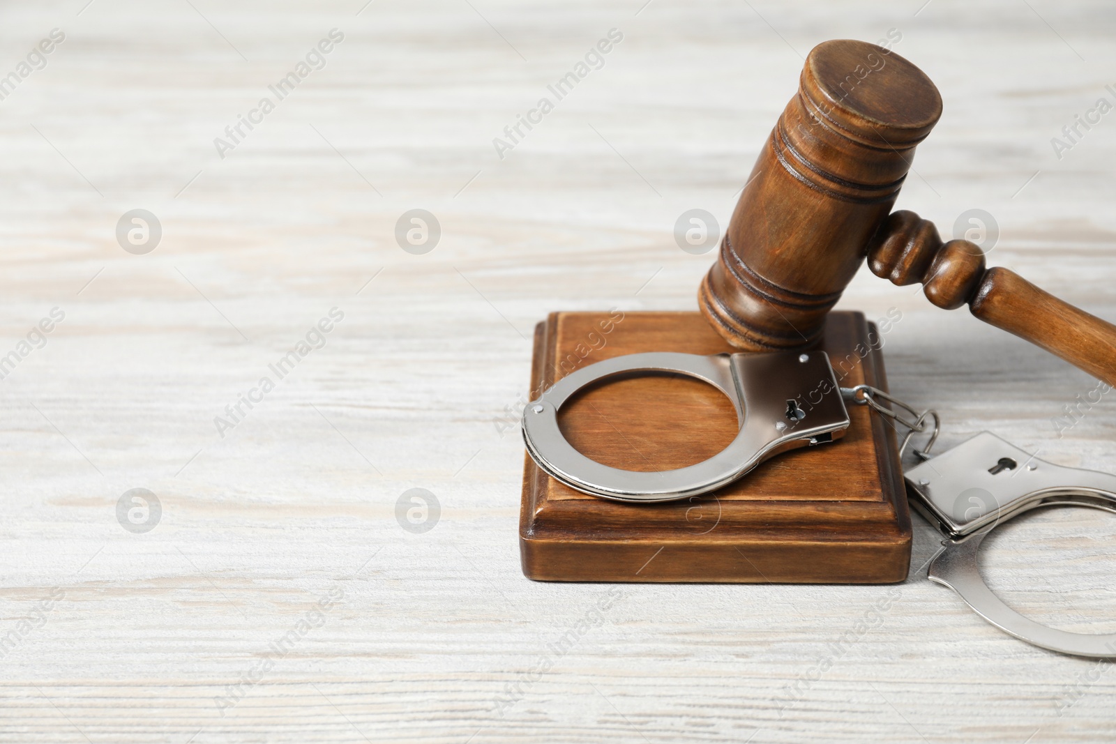 Photo of Handcuffs and judge's gavel on white wooden table. Space for text