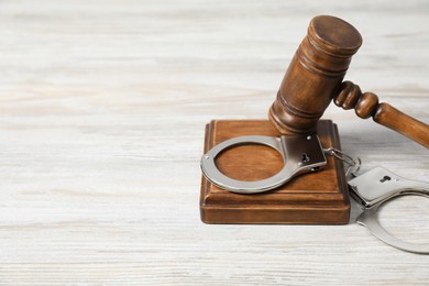 Photo of Handcuffs and judge's gavel on white wooden table. Space for text