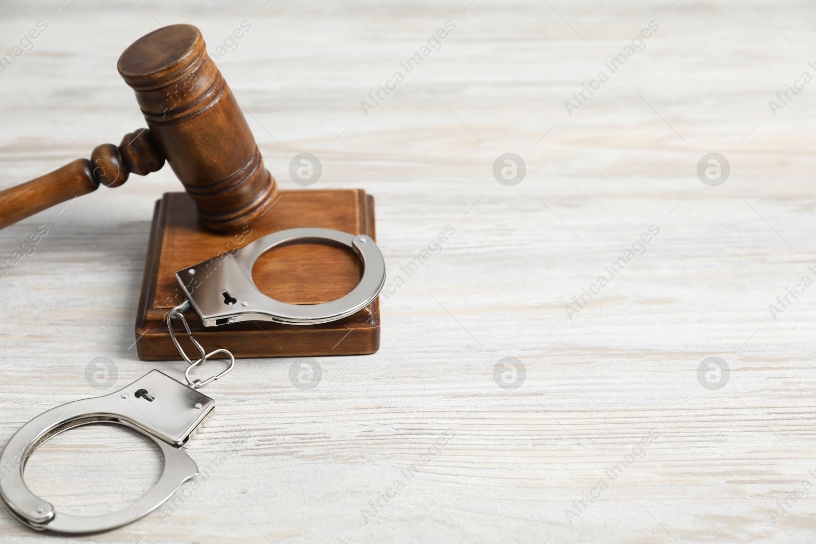 Photo of Handcuffs and judge's gavel on white wooden table. Space for text