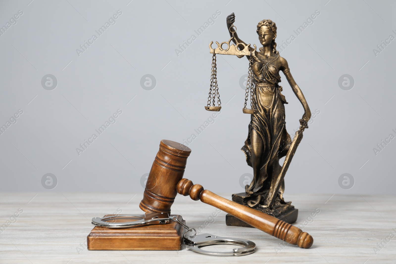 Photo of Handcuffs, judge's gavel and Lady Justice figure on white wooden table