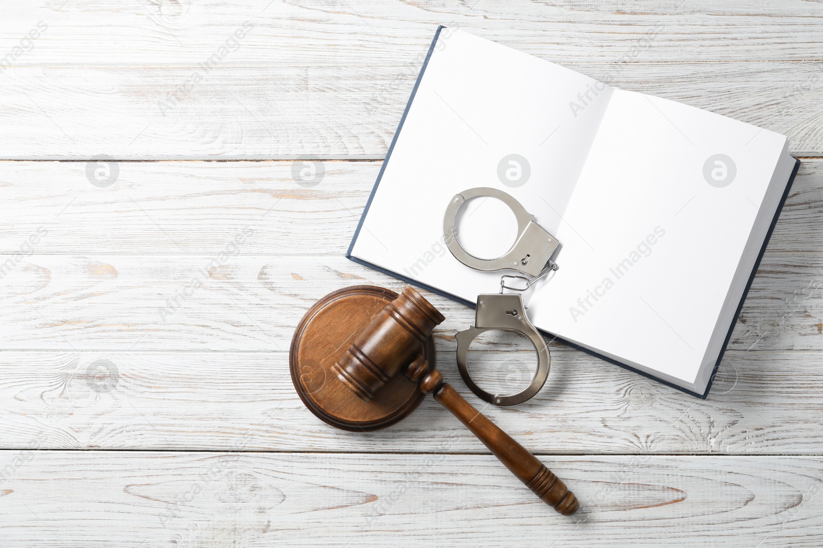 Photo of Handcuffs, judge's gavel and book on white wooden table, flat lay. Space for text