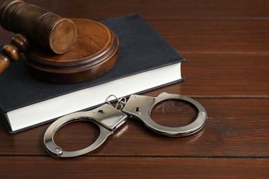 Photo of Handcuffs, judge's gavel and book on wooden table