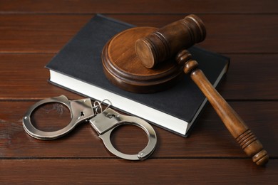 Photo of Handcuffs, judge's gavel and book on wooden table