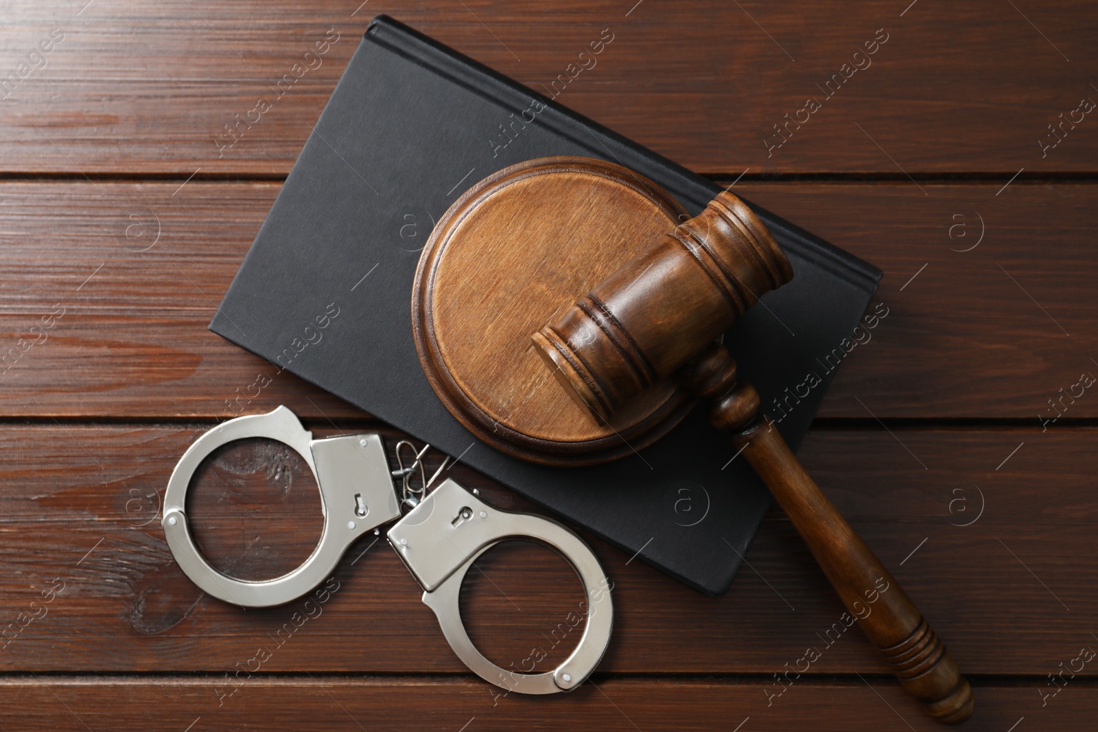 Photo of Handcuffs, judge's gavel and book on wooden table, flat lay