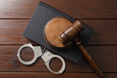 Photo of Handcuffs, judge's gavel and book on wooden table, flat lay