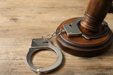 Photo of Handcuffs and judge's gavel on wooden table, closeup