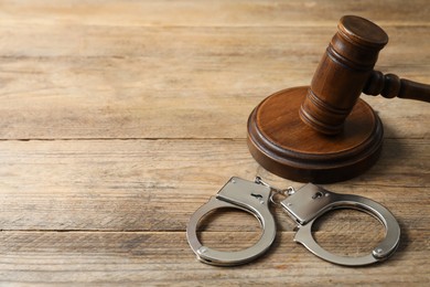 Photo of Handcuffs and judge's gavel on wooden table, space for text