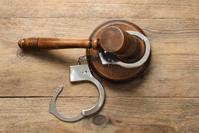 Photo of Handcuffs and judge's gavel on wooden table, flat lay