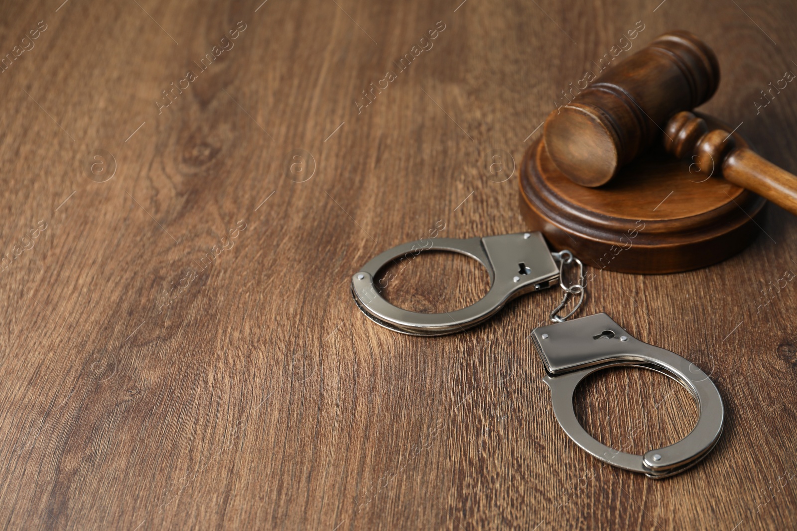 Photo of Handcuffs and judge's gavel on wooden table, space for text