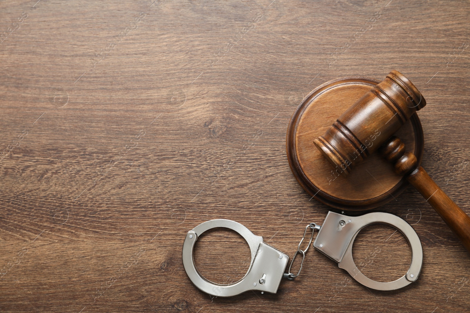 Photo of Handcuffs and judge's gavel on wooden table, flat lay. Space for text