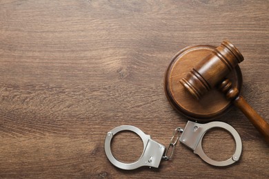 Photo of Handcuffs and judge's gavel on wooden table, flat lay. Space for text