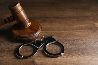 Photo of Handcuffs and judge's gavel on wooden table, space for text