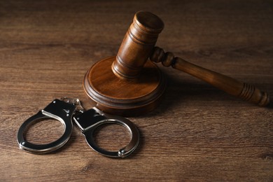 Photo of Handcuffs and judge's gavel on wooden table