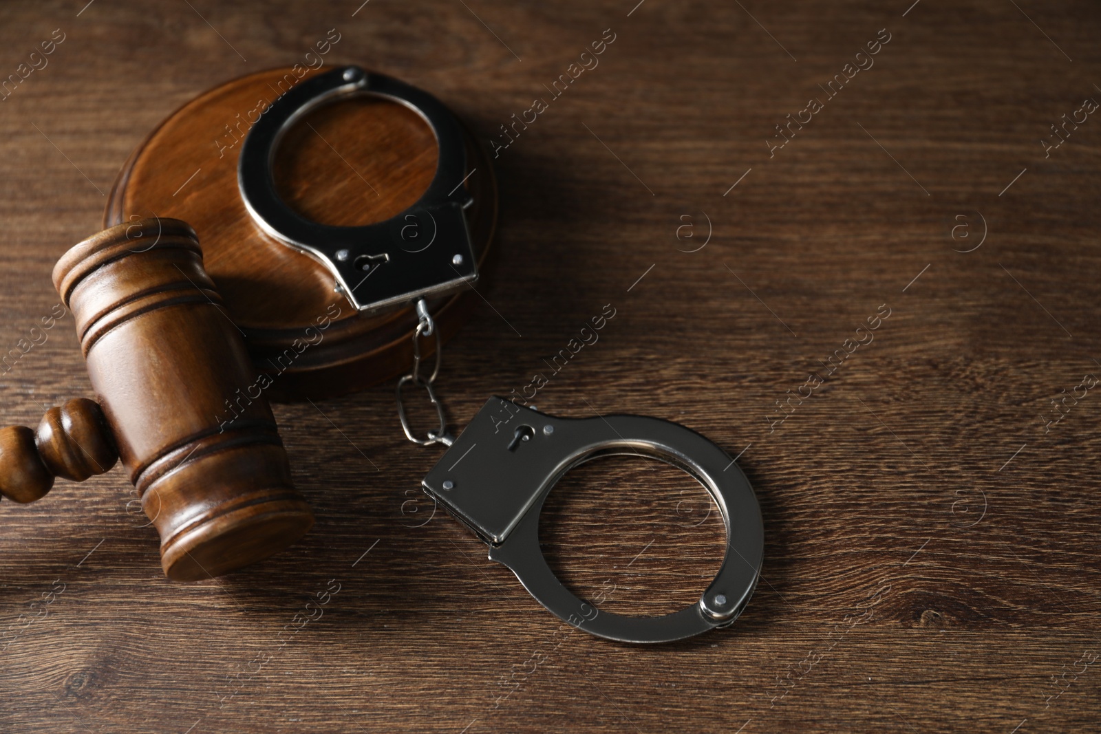 Photo of Handcuffs and judge's gavel on wooden table, space for text