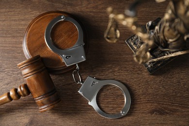 Photo of Handcuffs, judge's gavel and Lady Justice figure on wooden table, flat lay