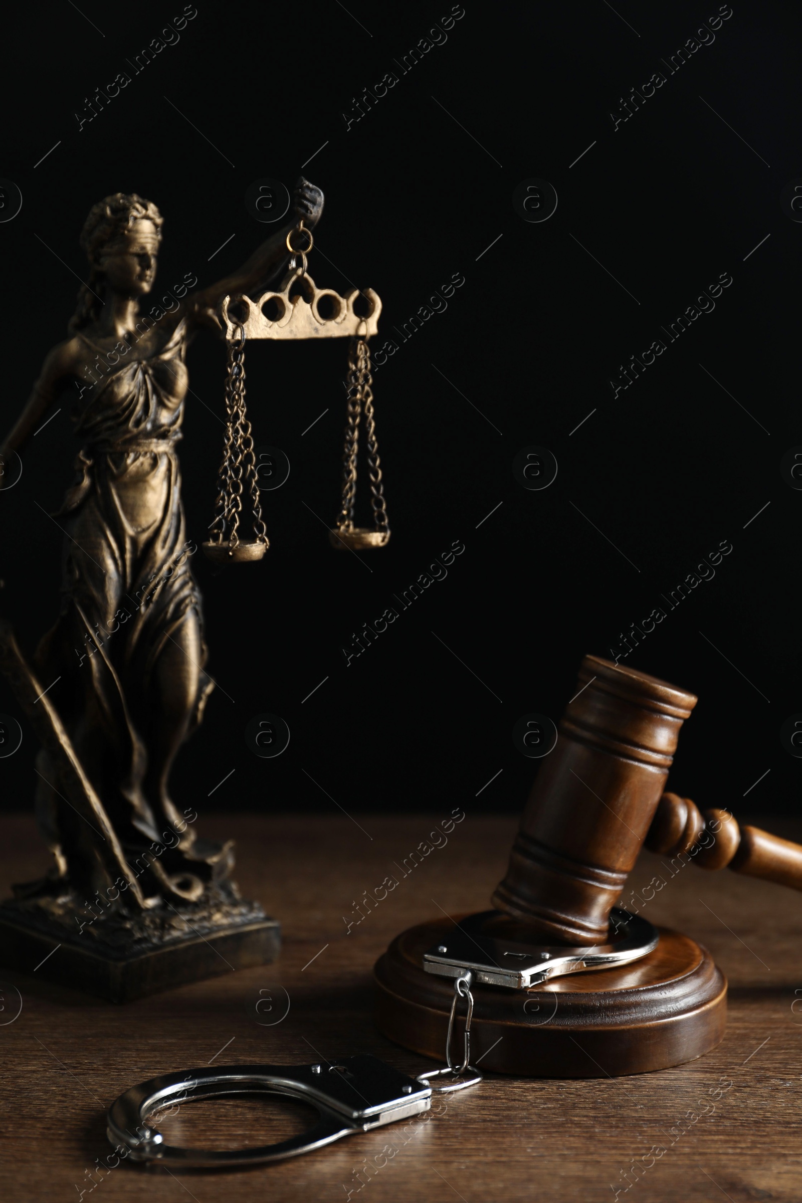 Photo of Handcuffs, judge's gavel and Lady Justice figure on wooden table