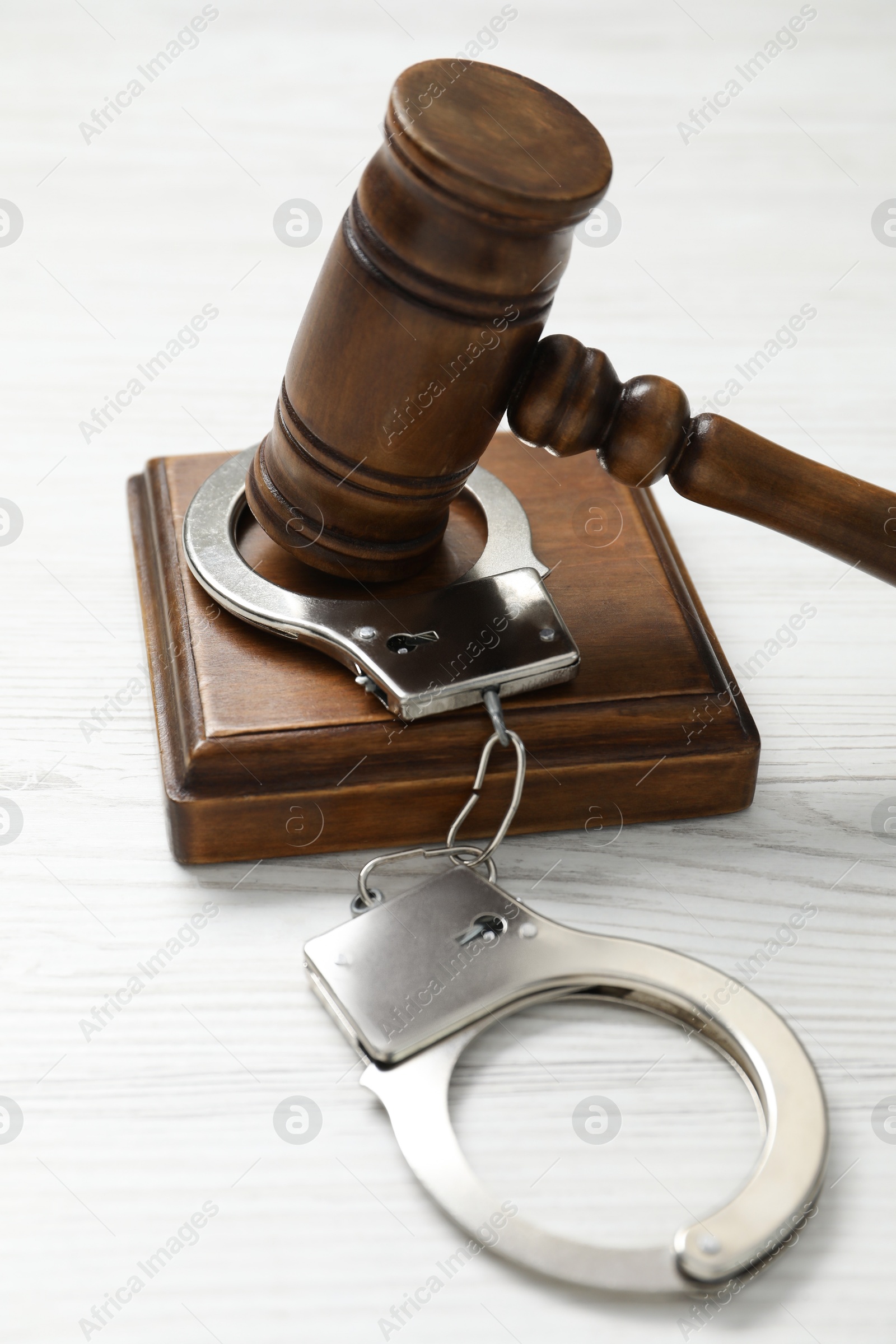 Photo of Handcuffs and judge's gavel on white wooden table, closeup